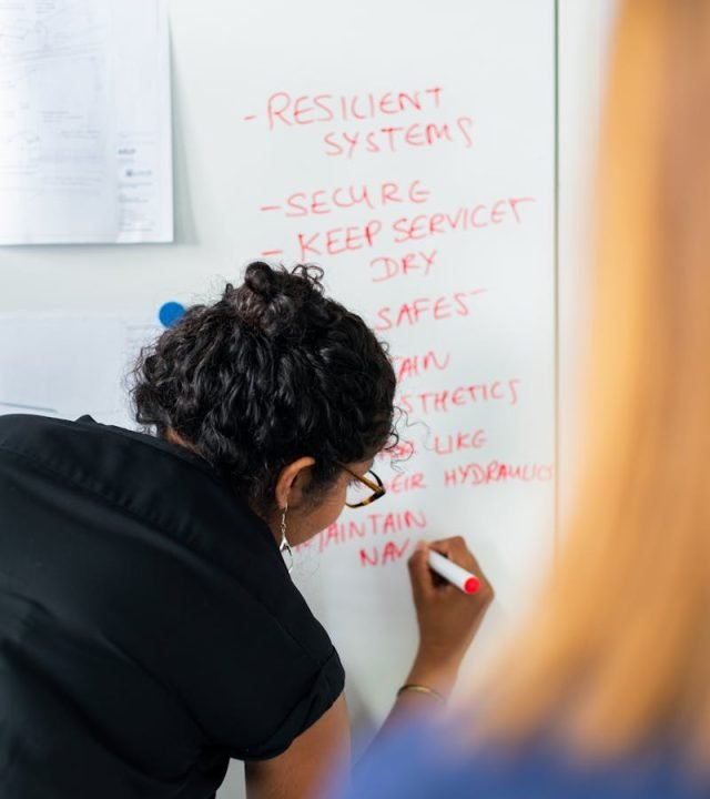 Female engineer writing strategy on a whiteboard during a business meeting.